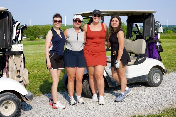 Four women golfers posing next to a golf cart on a gravel path at Ironwood