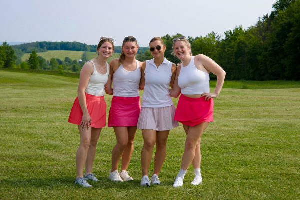 Four women golfers posing on the course wearing white tops and pink skirts