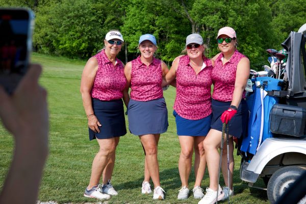 Four women golfers in matching pink tops and navy skirts posing beside a golf cart