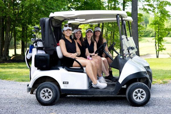Women golfers holding drinks beside golf cart on course